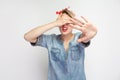 I don`t want to see this. Portrait of scared young woman in casual blue denim shirt and red headband standing, covering her eyes Royalty Free Stock Photo