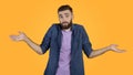 I don't know. Handsome Caucasian guy shrugging shoulders, feeling puzzled or uncertain on orange studio background