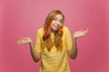 I dont know. Puzzled pretty positive young girl shrugging shoulders unsure in answer smiling on pink studio background