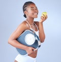 I feel blessed with good health. Studio shot of a young woman eating an apple and holding weighing scale under her arm. Royalty Free Stock Photo