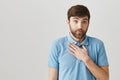 I feel like clearing my throat. Portrait of doubtful caucasian bearded guy holding palm on chest and looking with