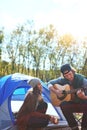 I fell in love with his music style. a young man playing his girlfriend a song on his guitar while out camping. Royalty Free Stock Photo