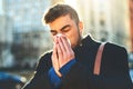 I hope this cold wont stop me from working. a irritated looking young man blowing his nose with a tissue while walking