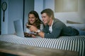 I know whats happening next...a young couple using their laptop together while lying on bed.