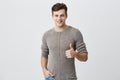 I like that. Good job. Happy caucasian male with dark hair wearing casual long sleeved sweater making thumbs up sign and