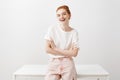 I like what you say. Attractive joyful european female with ginger hair in stylish pink jeans, leaning on table and