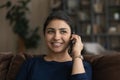 Positive millennial hindu woman relax on couch chat on phone