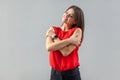 I live myself. Portrait of happy beautiful brunette young woman in red shirt standing, toothy smile and hugging herself and Royalty Free Stock Photo