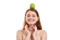 I love healthy food. Young playful red-haired girl holding a green apple on her head and smiling at camera while Royalty Free Stock Photo