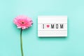 I love mom text and pink gerbera flower on turquoise background.