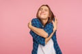 I love myself! Portrait of charming girl in checkered shirt hugging herself tightly and smiling with pleasure