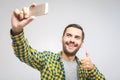 Handsome young man in shirt holding camera and making selfie and smiling while standing against grey background Royalty Free Stock Photo