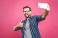 I love selfie! Handsome young man in shirt holding camera and making selfie and smiling while standing against pink background. Royalty Free Stock Photo