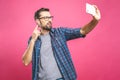 I love selfie! Handsome young man in shirt holding camera and making selfie and smiling while standing against pink background.