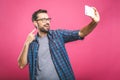 I love selfie! Handsome young man in shirt holding camera and making selfie and smiling while standing against pink background. Royalty Free Stock Photo
