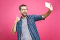 I love selfie! Handsome young man in shirt holding camera and making selfie and smiling while standing against pink background.