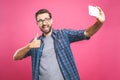 I love selfie! Handsome young man in shirt holding camera and making selfie and smiling while standing against pink background. Royalty Free Stock Photo