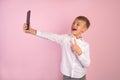 I love selfie. Handsome young schoolboy in shirt holding camera and making selfie and smiling while standing against pink