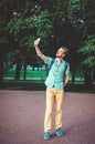 I love selfie. Outdoor summer lifestyle portrait of young bearded man holding camera and making . Smiling hipster guy in shirt