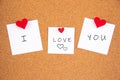 I love you handwriting lettering on 3 white papers pinned with 2 big red heart pegs and one small red heart pegs on cork board Royalty Free Stock Photo