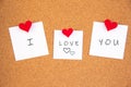 I love you handwriting lettering on 3 white papers pinned with 2 small red heart pegs and one big red heart pegs on cork board