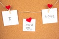 I love you lettering on 3 white paper pinned with 2 small red heart pegs and one big red heart pegs on cork board Royalty Free Stock Photo