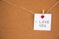 I love you lettering written on white paper pinned with small felt-hearted latch on cork board