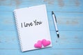I LOVE YOU word on notebook and pen with couple pink heart shape decoration on blue wooden table background. Wedding, Romantic and Royalty Free Stock Photo
