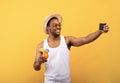 I'm on vacation. Smiling black guy in summer wear taking selfie with tropical fruit cocktail on yellow studio background