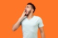 I need rest. Portrait of sleepy brunette man yawning and covering mouth with hand. isolated on orange background