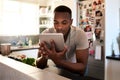 I need to find some good cooking videos. a handsome young man using a digital tablet while making breakfast in his Royalty Free Stock Photo