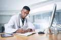 I need to follow up on this patient. a handsome young doctor sitting alone in his office at the clinic and writing in Royalty Free Stock Photo