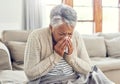 I need to go the see the doctor now. a sickly senior woman blowing her nose with a tissue while sitting on a sofa ta Royalty Free Stock Photo