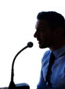 I need to make one thing clear...Sihouette shot of a man in a shirt and tie speaking into a microphone. Royalty Free Stock Photo