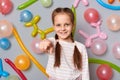 I need you. Smiling cute little girl with pigtails pointing to camera inviting you to her birthday party standing against gray
