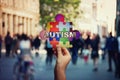 Symbol of Autism as a child hand holding a colorful puzzle piece over a crowded street background Royalty Free Stock Photo