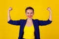 I am powerful and happy. Portrait of a happy elegant business woman showing power her biceps on yellow background. Multicultural