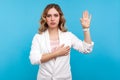 I promise. Portrait of beautiful woman making swearing gesture and holding arm on chest. blue background Royalty Free Stock Photo