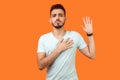 I promise. Portrait of serious brunette man standing with raised hand. studio shot isolated on orange background Royalty Free Stock Photo