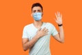 I promise. Portrait of serious brunette man with surgical medical mask standing with raised arm, swearing allegiance, taking oath