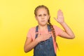 I promise to be honest! Portrait of serious responsible little girl with braid in denim overalls raising palm to take oath