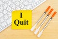 I quit message with disposable vaccine needle on desk with keyboard with a sticky note
