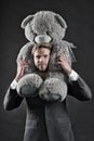 I am so sorry. Man carries giant teddy bear on neck, dark background. Reunion gift concept. Guy calm bearded face with