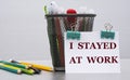 I STAYED AT WORK - words on a white sheet with clamps against the background of a cactus and jars with pencils