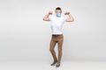 I am strong. Full length portrait of young man in white shirt with surgical medical mask standing and showing his biceps and