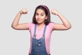 I am strong. Portrait of satisfied brunette young girl in casual pink t-shirt and blue overalls standing with raised arms and