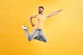 I am a superman! A young man dressed in a yellow T-shirt and light jeans jumps against a yellow wall, straightening one hand