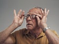 I think I need a new lens. Studio shot of an elderly man adjusting his spectacles against a grey background.