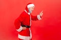 I told you! Side view of elderly man with gray beard wearing santa claus costume standing with attention sign, with finger warning