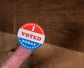 I Voted Today paper sticker on mans finger on rustic wooden table